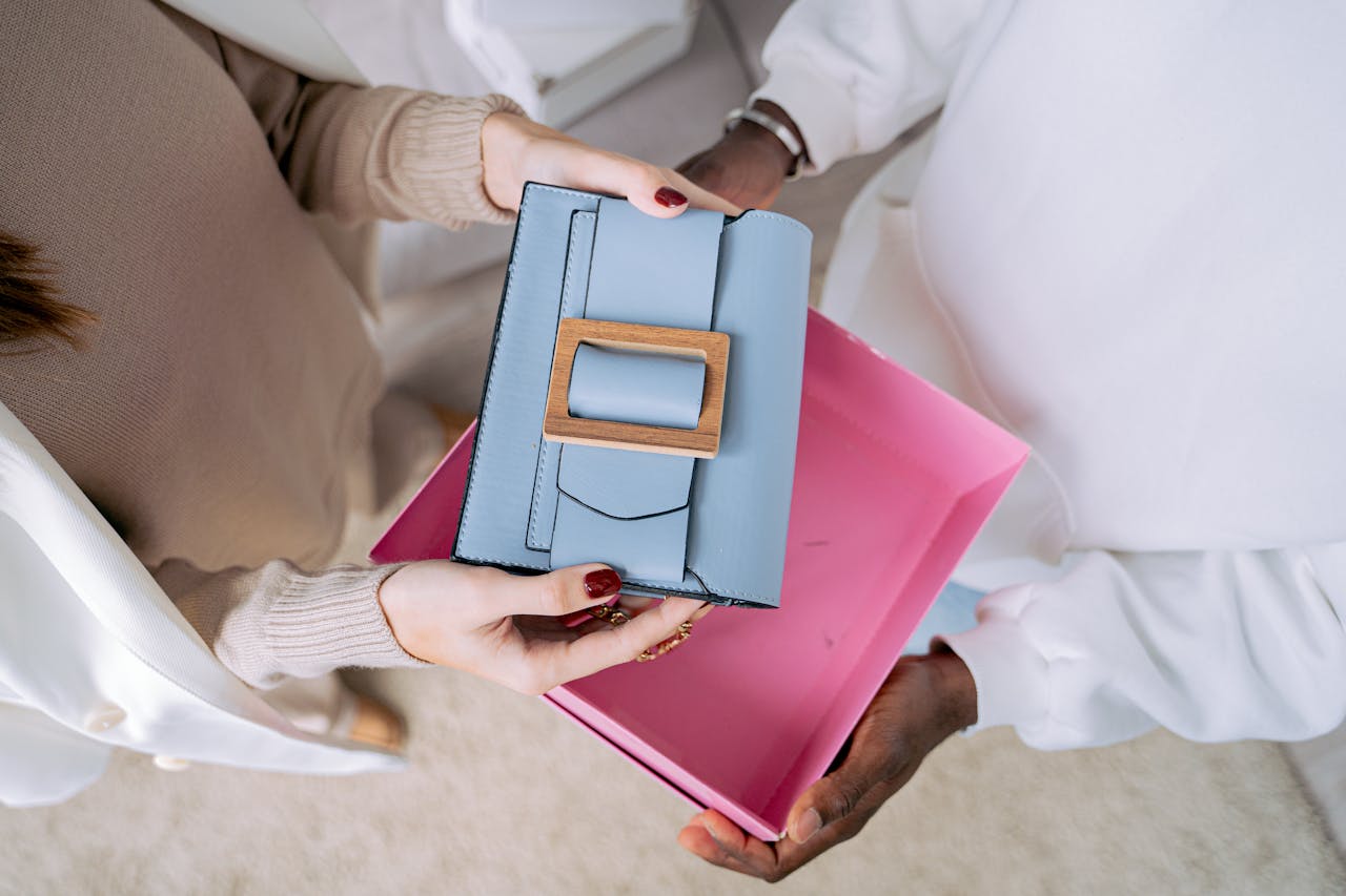 Close-up of a stylish blue handbag being given as a gift in a vibrant pink box.